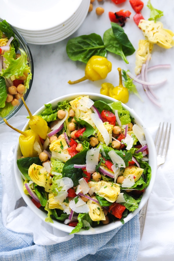 Green salad in a bowl with chickpeas, pepperoncini peppers, red peppers, artichokes and diced onions.