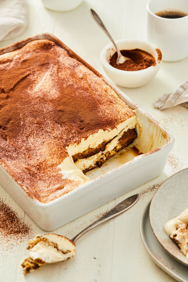 Tiramisu in dish with espresso powder and a cup of coffee