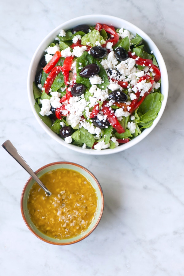 Pepperoncini vinaigrette dressing in a bowl next to a salad with feta, olives and peppers