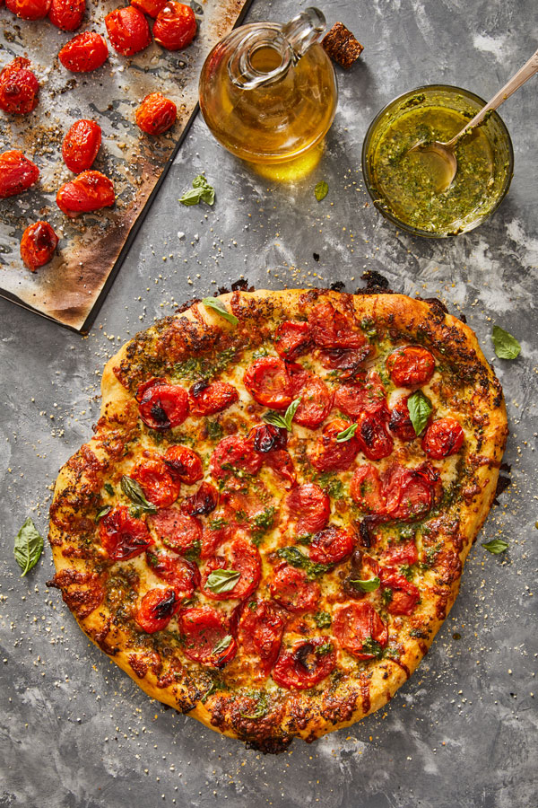 Baked pizza with charred tomatoes, pesto sauce and torn fresh basil leaves.