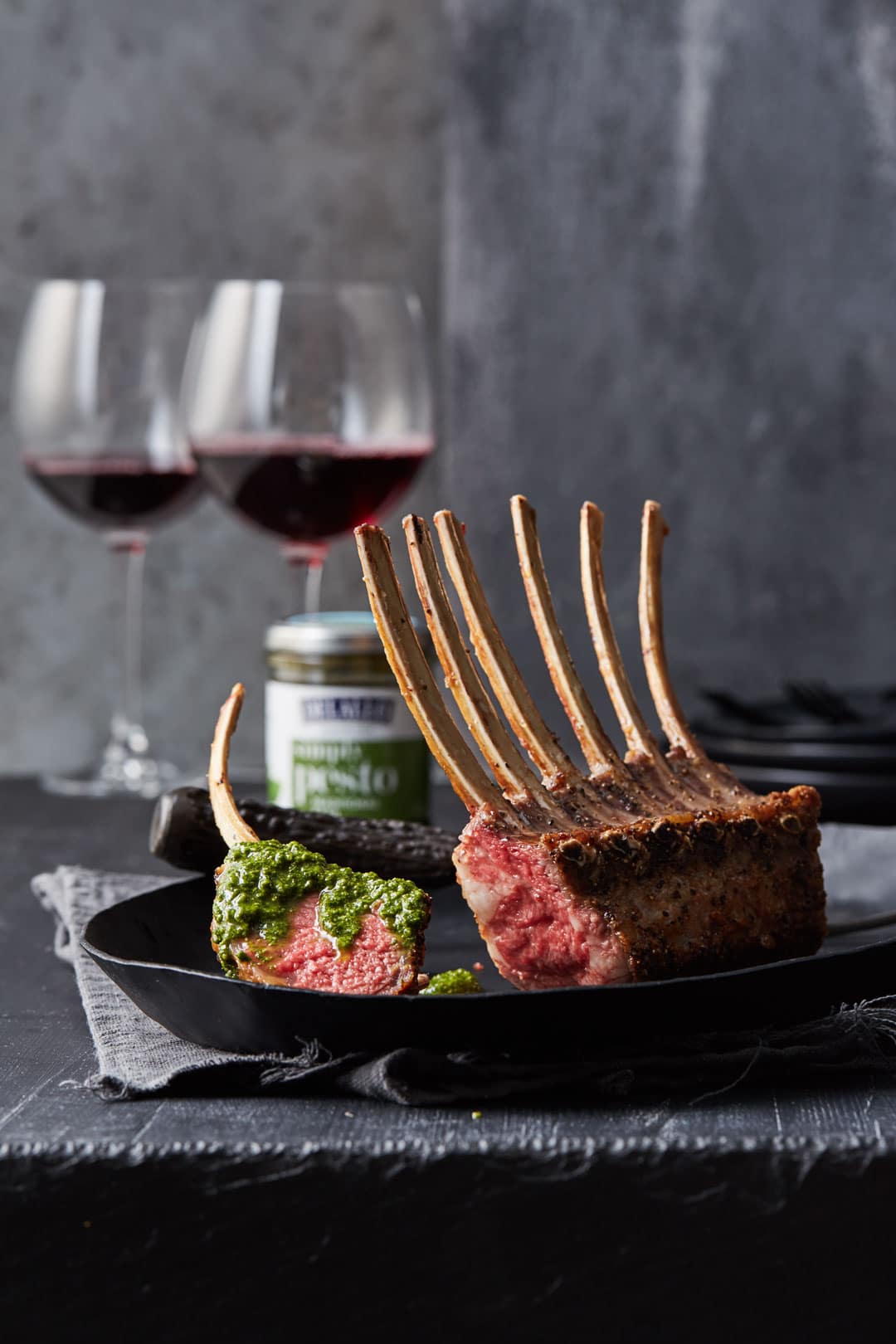 A rack of lamb ribs served on a plate with pesto. The ribs are served with wine. 