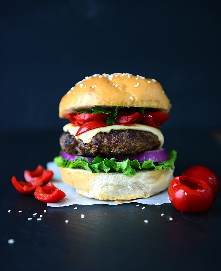 Angus beef burger topped with sharp cheddar and red pepperazzi peppers in between a sesame bun  