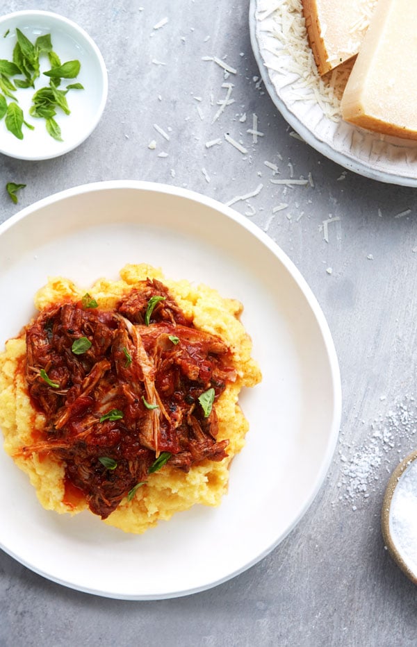 Polenta topped with pulled pork in a red sauce and served on a plate