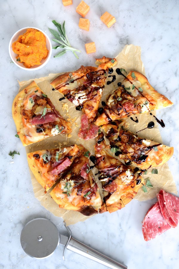 Baked pizza topped with sweet potatoes and sliced sopressata and drizzled with balsamic glaze