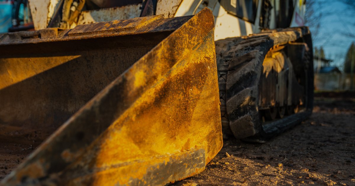 A compact track loader is in the middle of an unpaved outdoor area with imprinted tracks, loading up a pile of dirt.