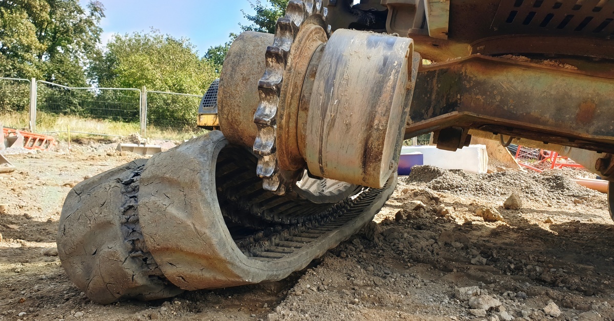 An excavator sits off-balance with one side of the machine lifted off the ground and rubber tracks hanging off it.