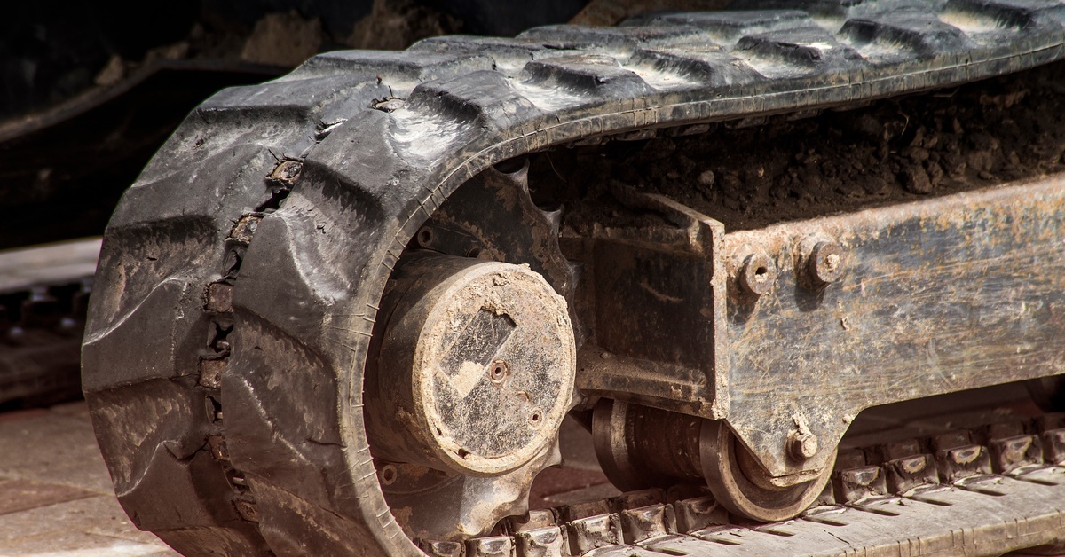 A close-up of the dirty, worn-out rubber tracks on a heavy industrial machine sitting outside on a brick surface.