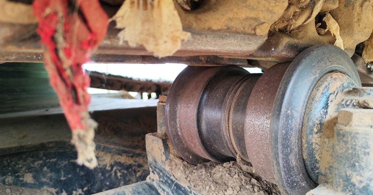 A close-up of the undercarriage of large machinery thickly packed with mud and pieces of fabric hanging from it.