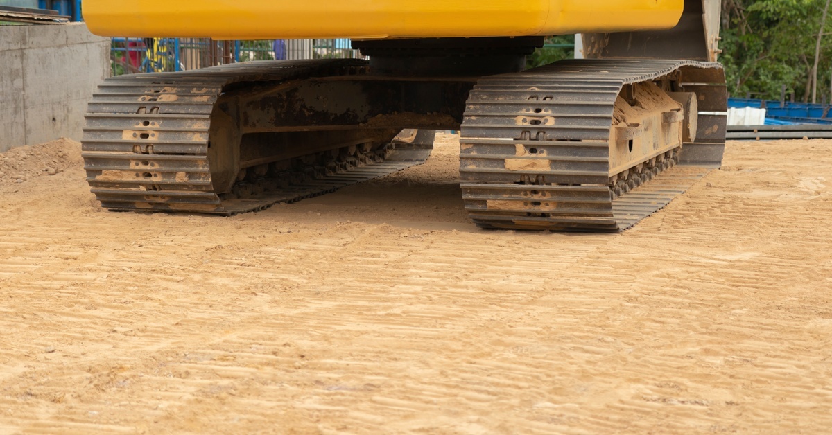 A close-up of the undercarriage of a large machine on a construction site with a dirt ground.