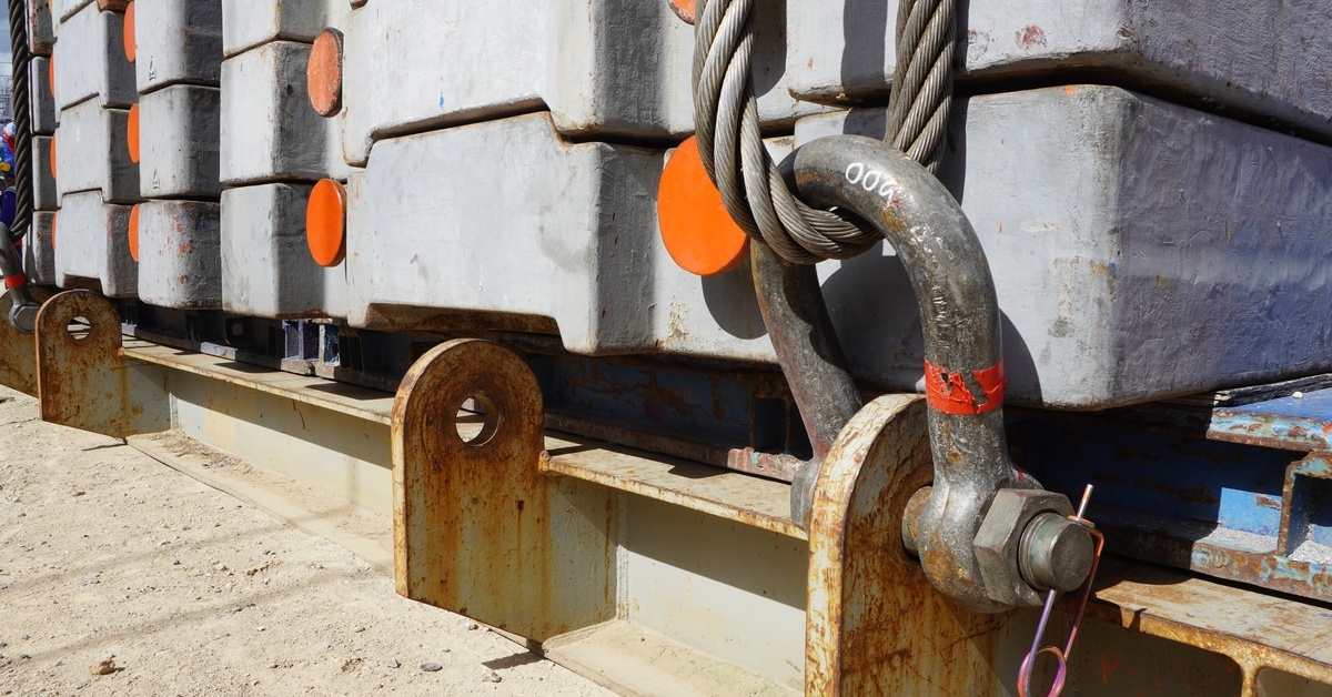 A close-up of thick grey counterweights stacked on top of each other and hooked down to an industrial surface outside.