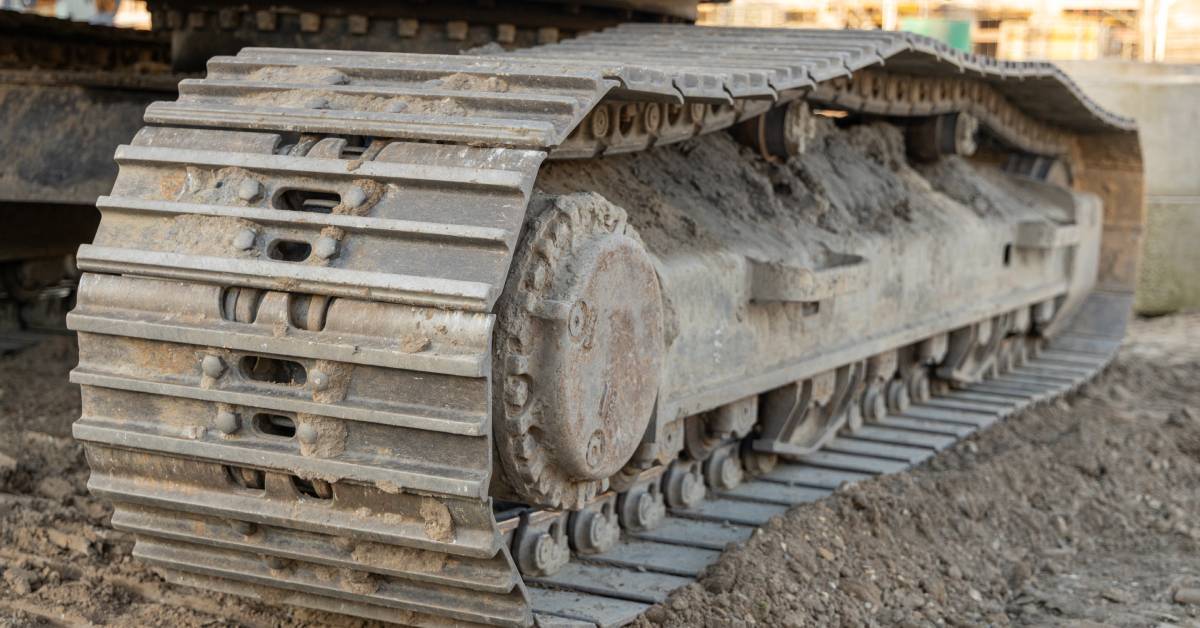 A close-up of dirt-impacted, rusted tracks on heavy machinery sitting on a muddy construction site.