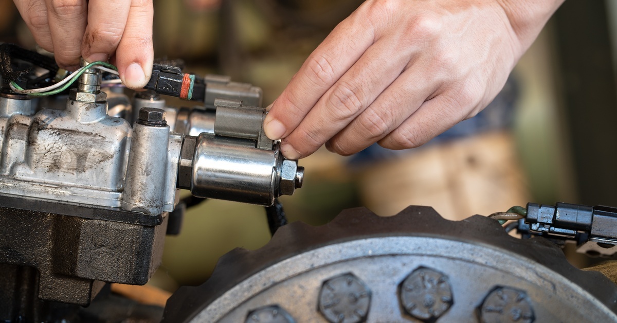 A close-up of a person holding wiring while working on the components of a large vehicle transmission.