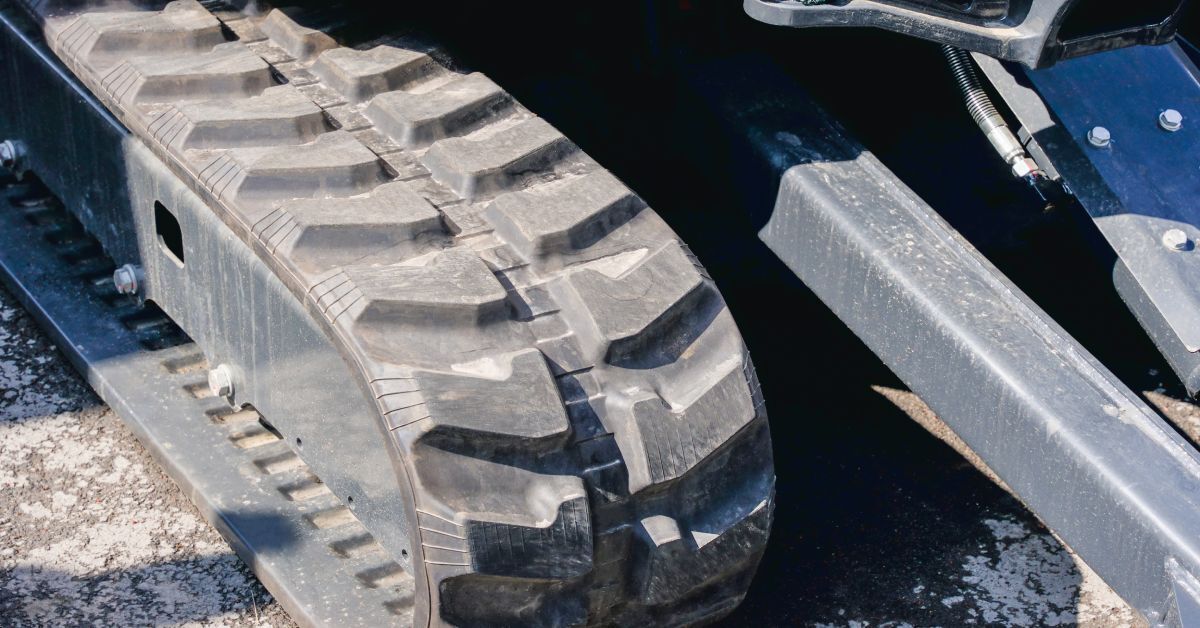 A close-up of the rubber tracks on a large yellow machine sitting on top of a cement surface outdoors.