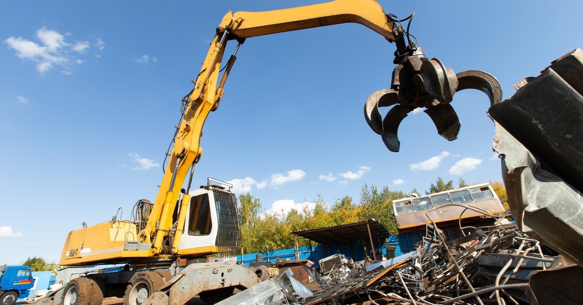 A truck with a large machine crane attachment picks up piles of metal debris at a construction site.