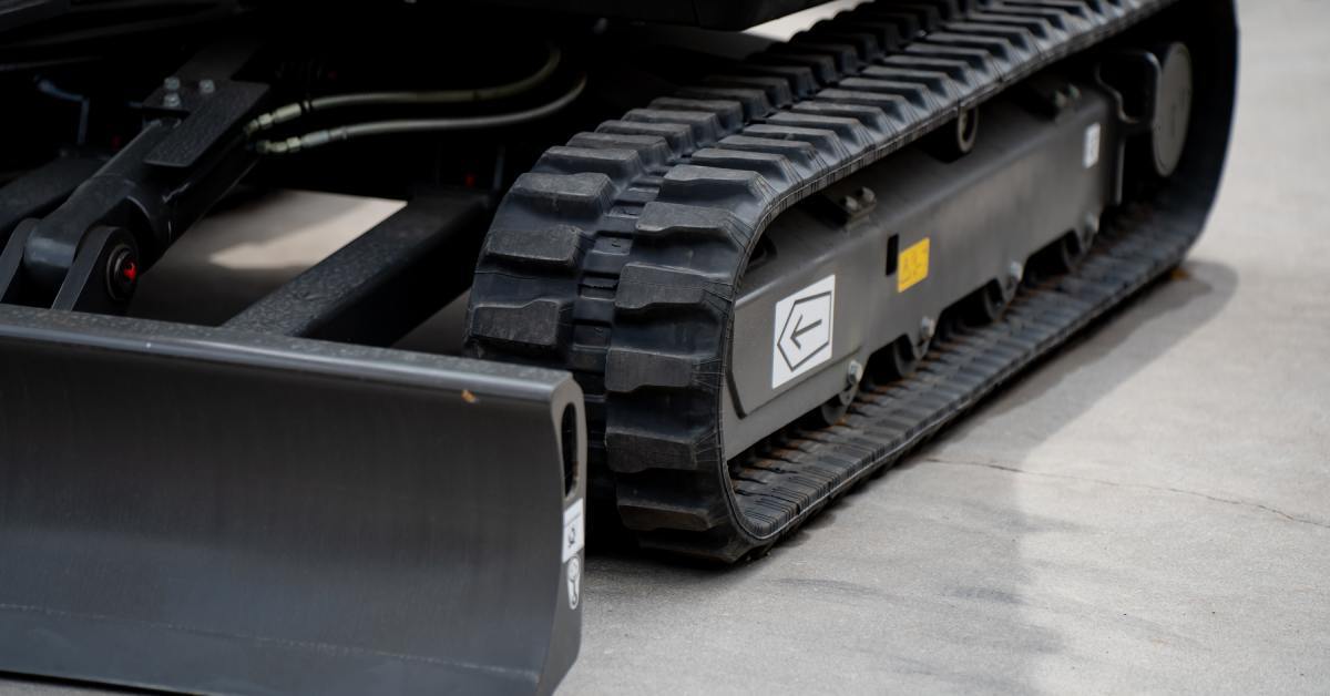 A close-up of rubber tracks on a heavy machine in a show room on a gray ground. They are in almost mint condition.
