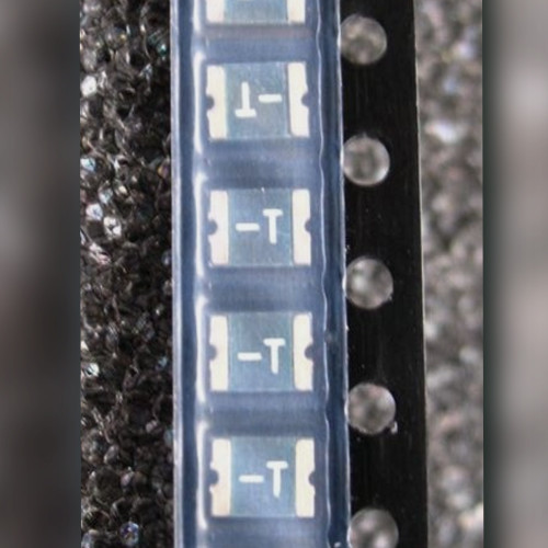 Carrier tape strip of resettable fuse chips marked -T on a dark speckled surface