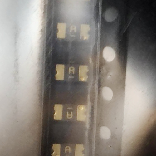Strip of dark chip resettable fuses marked A in black carrier tape under clear cover tape