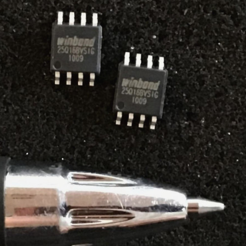 Two Winbond SOIC-8 flash chips marked 25Q16BVSIG on a dark textured surface beside a pen tip