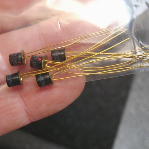 Five black TO-1 metal can units with gold leads; partial markings 2N228 visible on bodies; red dot visible on two units.
