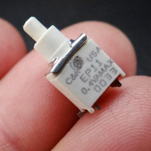 White plastic SMT body marked C&K USA, EP11, 0.4VA MAX, and code 003. Silver metal actuator bar visible. Six SMT pins present, no visible damage.