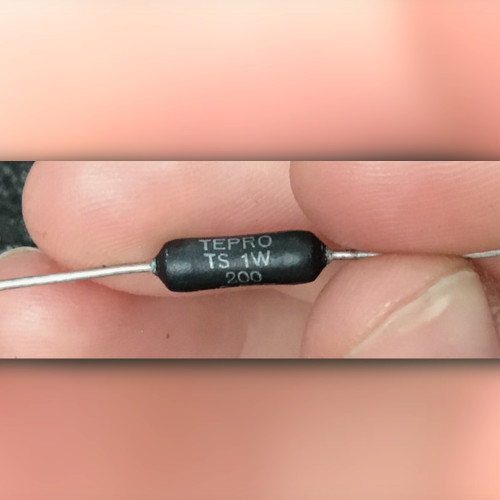 Fingers hold black axial resistor printed TEPRO TS 1W above 200, dark speckled backdrop
