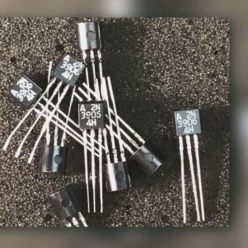 Several black TO-92 transistors scattered on a dark speckled surface, bodies marked A 2N3906 4H