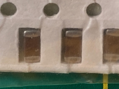 Three amber brown chip capacitors in tape, slightly soft focus, green mat below