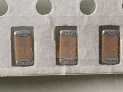 Macro of three tan ceramic chip capacitors with silver end caps in tape