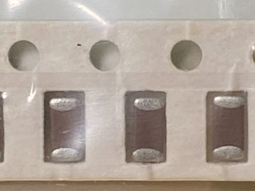 Three chip capacitors with oval silver end terminations seated in white paper tape