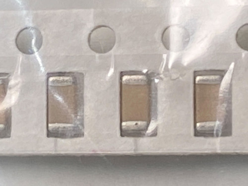 Three pale tan chip capacitors in tape with wrinkled bag film peaked between pockets
