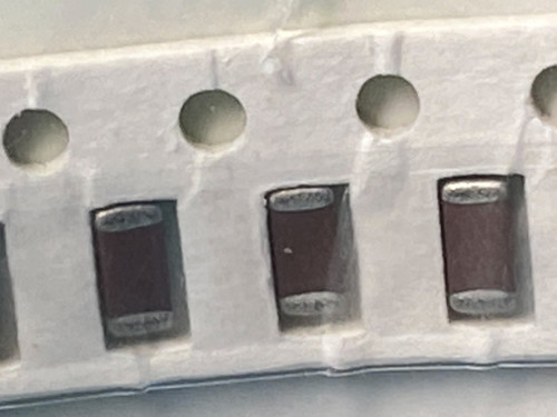 Tilted tape with three dark maroon chip capacitors and large sprocket holes above