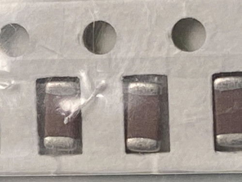 Three dark brown chip capacitors in tape, bag film crumpled over the left one