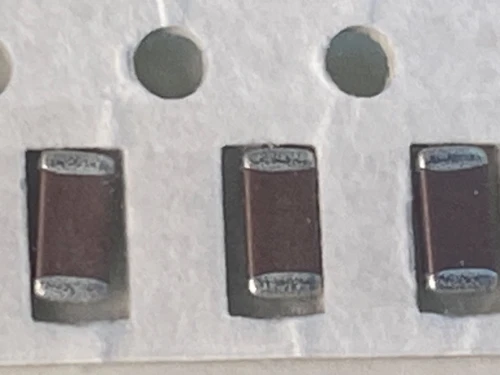 Macro of three dark maroon chip capacitors in tape, cut paper edge along bottom