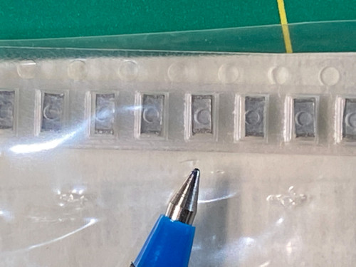 Eight small gray SMD film capacitors held in clear carrier tape on white backing