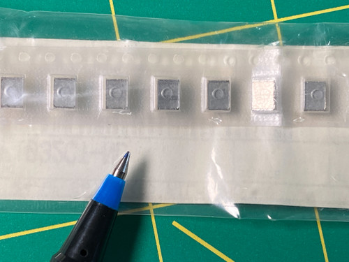 Seven film chip capacitors in bagged carrier tape on green mat, one cream colored