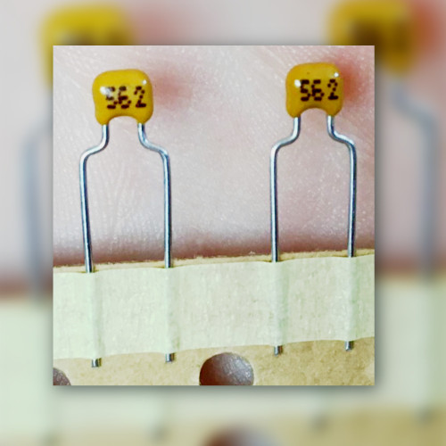 Two yellow radial ceramic capacitors marked 562 on carrier tape.