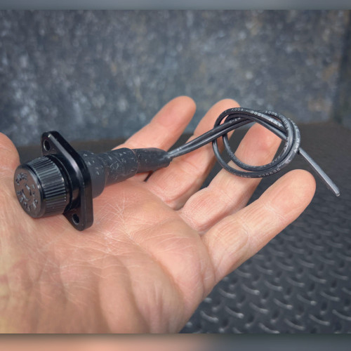 Black fuse holder with knurled cap, two-hole flange, and coiled leads in palm