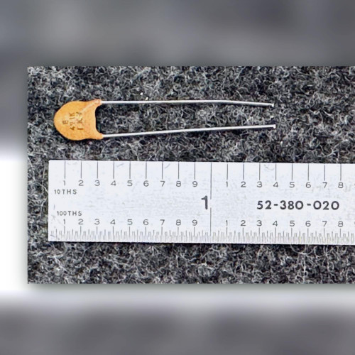 Orange-tan ceramic disc capacitor beside a steel inch ruler on a dark speckled mat