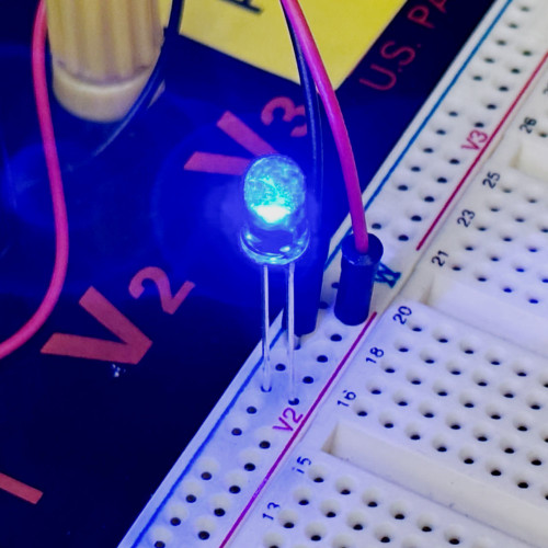 Close-up of unbranded 073118A1155 5mm blue LED powered and illuminated on a breadboard.