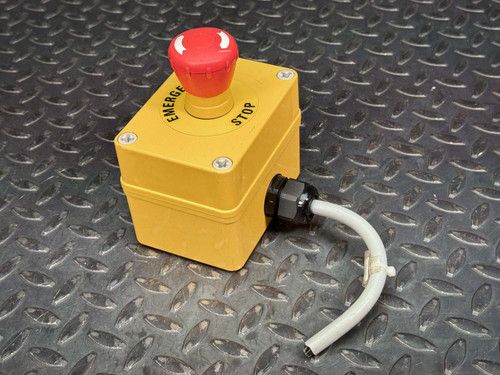A yellow EMO e-stop - Allen-Bradley emergency stop box with a prominent red mushroom button, connected to a bent grey cable through a black cable gland. The device is placed on a textured diamond plate metal surface, indicating a ready-to-use setup for safety operations.