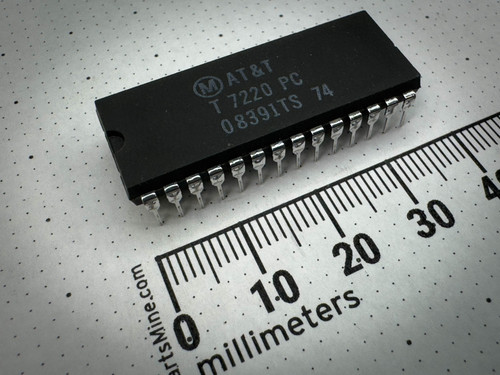 Angled view of an AT&T T7220 PC microchip featuring multiple metallic pins, alongside a ruler for scale marked in millimeters on a dotted white background.