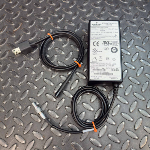 Overhead view of an Emerson DP4012N2M AC Power Adapter with 4-Pin Lemo Plug from PartsMine.com, featuring its cords neatly coiled with orange ties, placed on a textured metal surface.