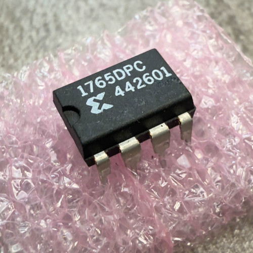Xilinx 1765DPC 8-Pin Serial EPROM IC from PartsMine.com, angled close-up of the black integrated circuit with white markings “1765DPC 442601,” resting on pink anti-static foam.