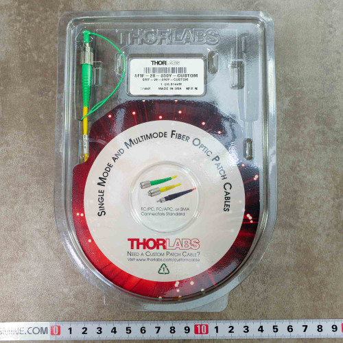 Thorlabs clamshell pack with factory label SMF-28-030Y-CUSTOM and green connector above metric ruler
