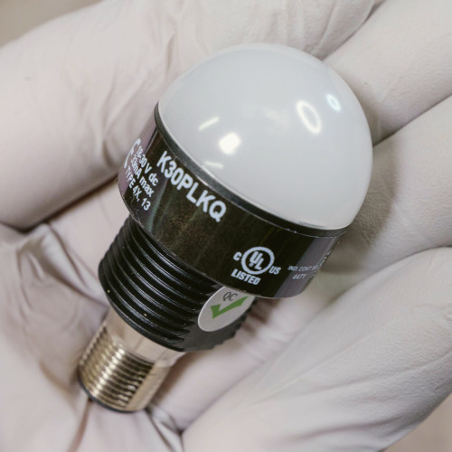 Gloved hand holding white dome LED indicator, label reads K30PLKQ, 18-30 V dc.