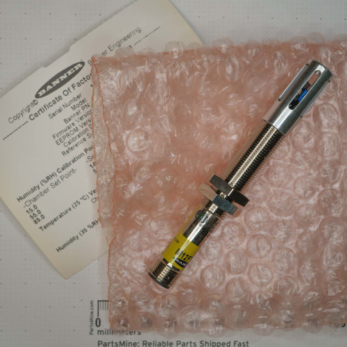 Banner sensor showing clean aluminum housing, intact threads, M12 connector, and yellow label. Includes partial "Certificate Of Factory" document.