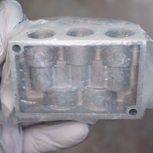 Cast aluminum body with three top ports and six internal bosses visible through face. Mounting holes at each corner. No visible damage or markings.