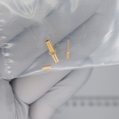 Three gold-plated contact pieces visible: one threaded barrel with hex flange and hollow bore, one slim pin with flanged head, one short ferrule sleeve.