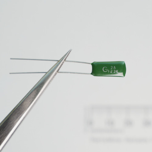 Unbranded 2A123K green radial film capacitor held in tweezers, displaying body markings.