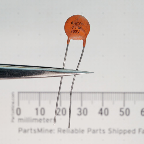 ARCO 100V.01M ceramic disc capacitor held in tweezers against a millimeter ruler.